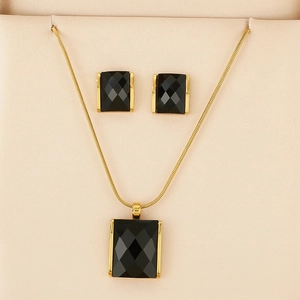 Detail of gold necklace and stud earrings set with black rectangular faceted gemstones