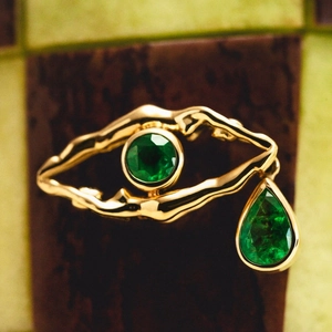 Golden evil eye necklace with emerald green round and teardrop stones on checkered background