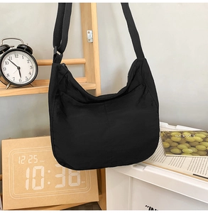 Close-up of a black nylon crescent crossbody bag hanging on a minimalist wooden rack