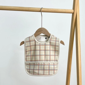 Waterproof baby bib with red and blue plaid pattern and food catcher on wood hanger