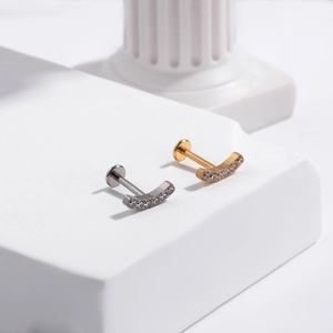 Detailed view of silver and gold curved ear studs with zircon gems on a white prop