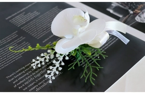 Close-up of elegant white orchid boutonniere with green foliage and cream ribbon on a magazine