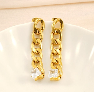Macro view of gold chain drop earrings with square zirconia stones on white ceramic
