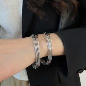 Close-up of minimalist layered silver wire bracelets on wrist over a black suit