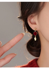 Close-up of red flocked round earrings with dangling gold metal discs on a female model