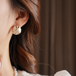 Detailed close-up of a white and gold spiral ball stud earring on a female model