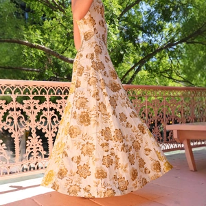 Detailed view of the flowy hem and golden floral print on a white bohemian maxi dress