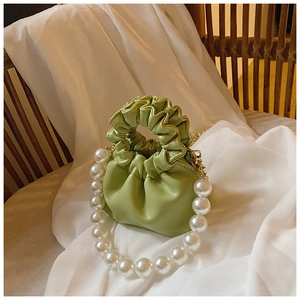 Detail view of light green ruched mini handbag featuring large pearl handle and gold chain