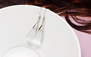 Detailed view of silver drop earrings with white cat-eye stones hanging on a ceramic bowl