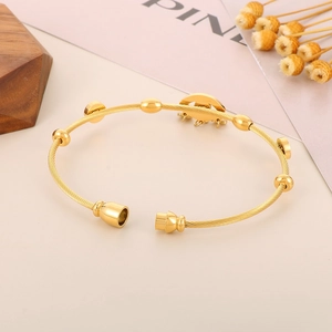 Detail of gold twisted cable cuff bracelet with metal beads and round charm on a desk