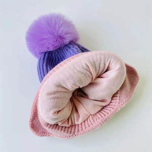 Detail of purple knit hat with plush pom-pom and soft pink fleece lining for warmth