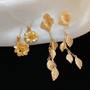 Macro shot of gold floral studs and leaf tassel earrings with a refined hammered texture