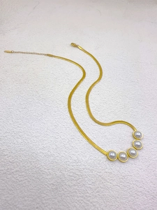 Detail of gold snake chain necklace featuring five white pearls on white background