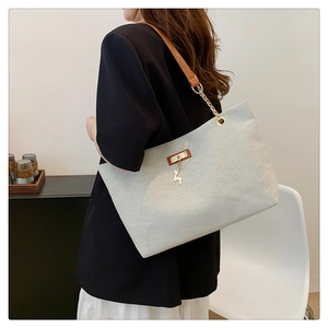Detail of light blue denim tote bag with brown leather strap and gold deer charm