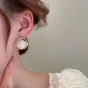 Detailed close-up of a gold irregular metal earring with a lustrous white pearl on a model