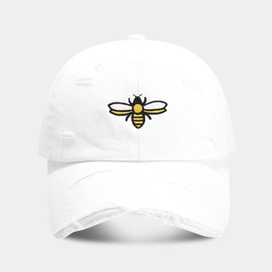 Close-up of yellow bee embroidery and distressed holes on white cotton baseball cap