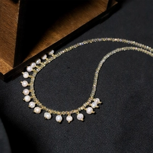 Detail of yellow crystal beads necklace with hanging white pearl pendants and gold accents