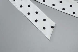 Close-up of vintage black polka dot belt on white fabric with diagonal flat lay