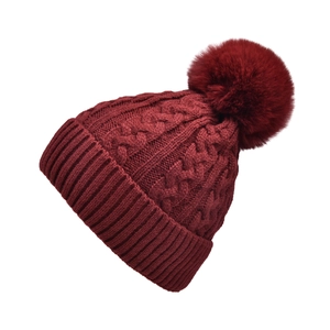 Close-up of wine red cable knit beanie with large faux fur pompom and ribbed cuff