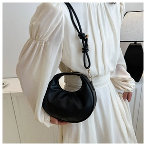 Detail of a minimalist black crescent leather handbag with shoulder strap on a white dress