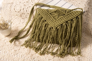 Detail der olivgrünen Makramee-Umhängetasche mit Boho-Fransen auf einer Spitzendecke