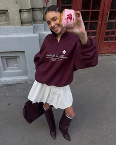 Outdoor shot of a burgundy half-zip sweatshirt paired with a white pleated mini skirt