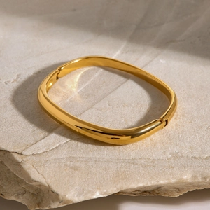 Macro di un bracciale rigido quadrato dorato lucido su uno sfondo in pietra naturale