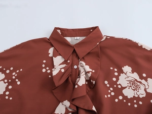 Détail du col d'un chemisier floral caramel avec volants élégants et bouton blanc