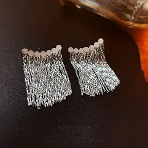Silver metallic chain tassel earrings with round rivet studs on dark leather background