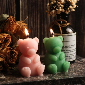 Pair of sitting bear-shaped scented candles in pink and green colors on a vintage desk