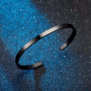 Detailed view of a sleek black C-shaped stainless steel bangle on a shimmering background