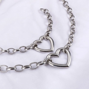 Detail of silver heart pendants on thick link chains against a white fabric backdrop