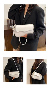Detail view of the white leather shoulder bag featuring a stylish wavy flap design