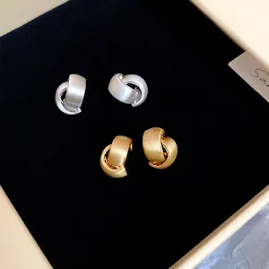 Matte gold and silver brushed metal C-shaped earrings in minimalist knot design