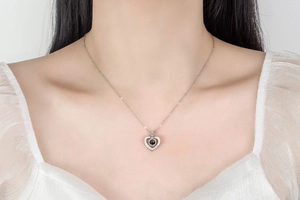 Close-up of heart pendant necklace on model showing 'LOVE' engraving and black bead