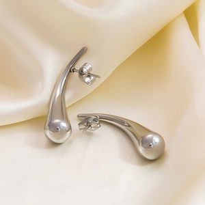 Close-up of silver hollow teardrop earrings on beige silk fabric with smooth metallic finish