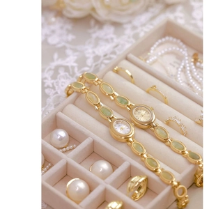 Elegant gold oval watch with green gemstone chain strap shown on a velvet jewelry box