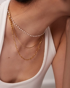 Close-up of triple-layered necklace featuring small pearls and gold chain on model neck