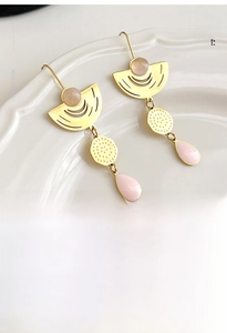 Detail of gold geometric drop earrings with pink crystal and enamel pendants in a dish