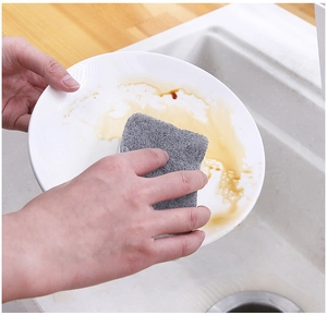 Close-up of a double-sided cleaning sponge removing grease from a white ceramic dish