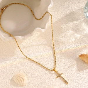 Detail of gold cross pendant with white crystals and rope chain on white texture