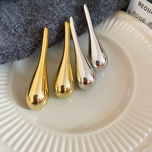 Close-up of polished gold and silver teardrop earrings on a white ribbed ceramic tray