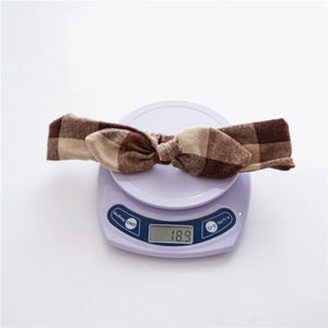 Detail shot showing 18.9g weight of brown plaid rabbit ear headband on a scale