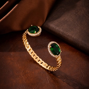 Detail of gold-tone open bangle with oval green gemstones and Cuban link chain texture