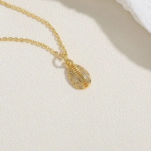 Detailed close-up of a gold rugby-shaped pendant necklace featuring inlaid zircon stones