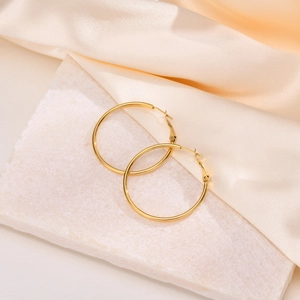 Macro detail of large gold-polished hoop earrings resting on marble and silk fabric