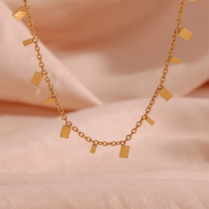 Macro detail of 18K gold-plated square sequins necklace on soft pink silk fabric