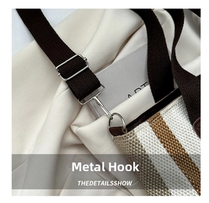 Close-up of silver metal hooks and adjustable strap on a striped woven tote bag