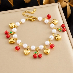 Detail of gold chain bracelet with pearls, cherry pendant and heart charm on display