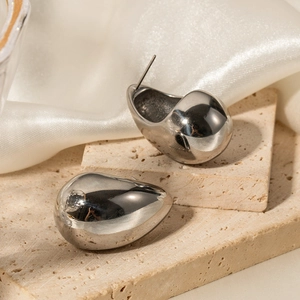 Macro detail of silver-tone teardrop earrings placed on beige travertine stone texture
